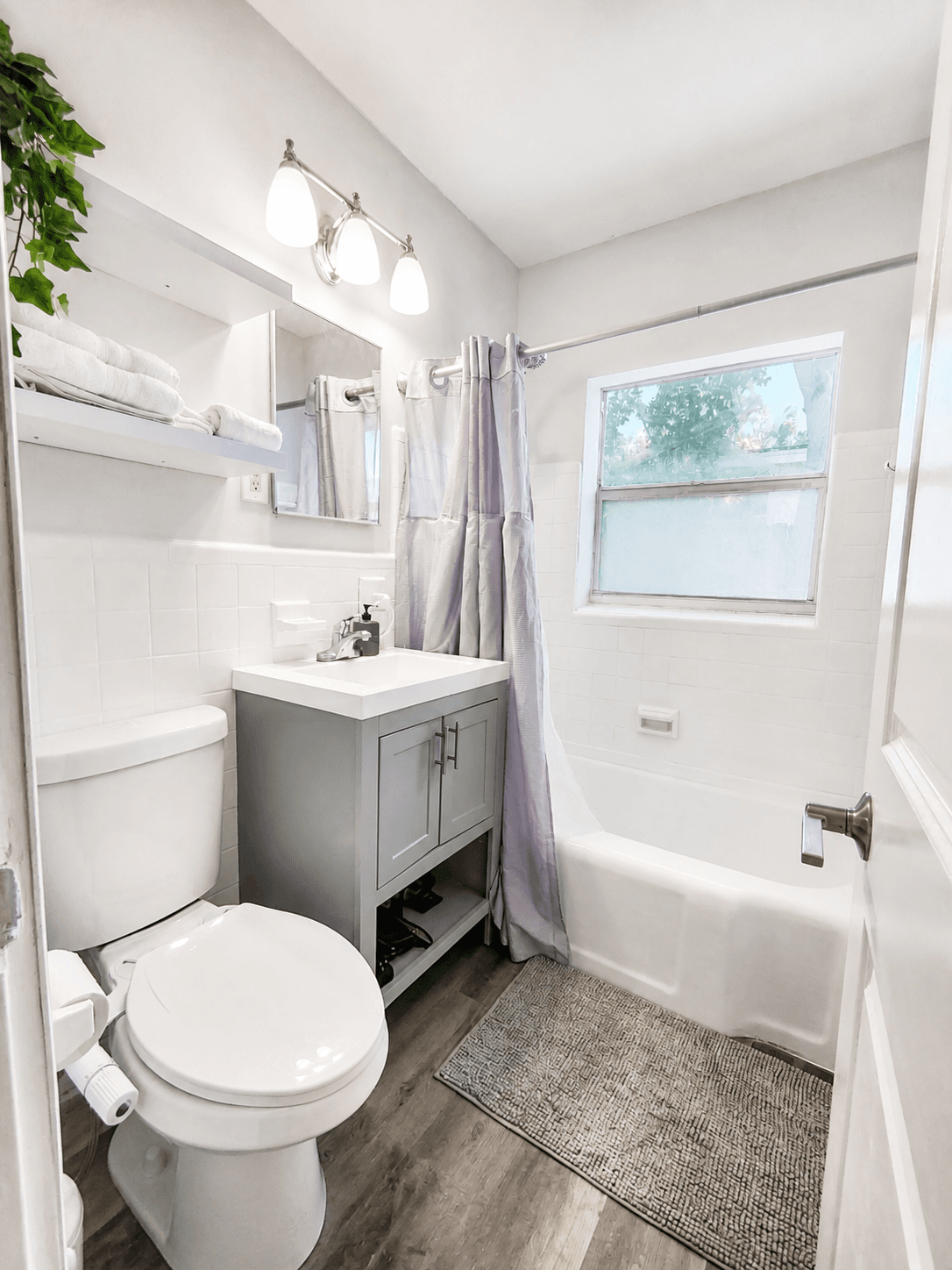 One-bedroom bathroom with grey vanity, bathtub shower combo, and towel shelf