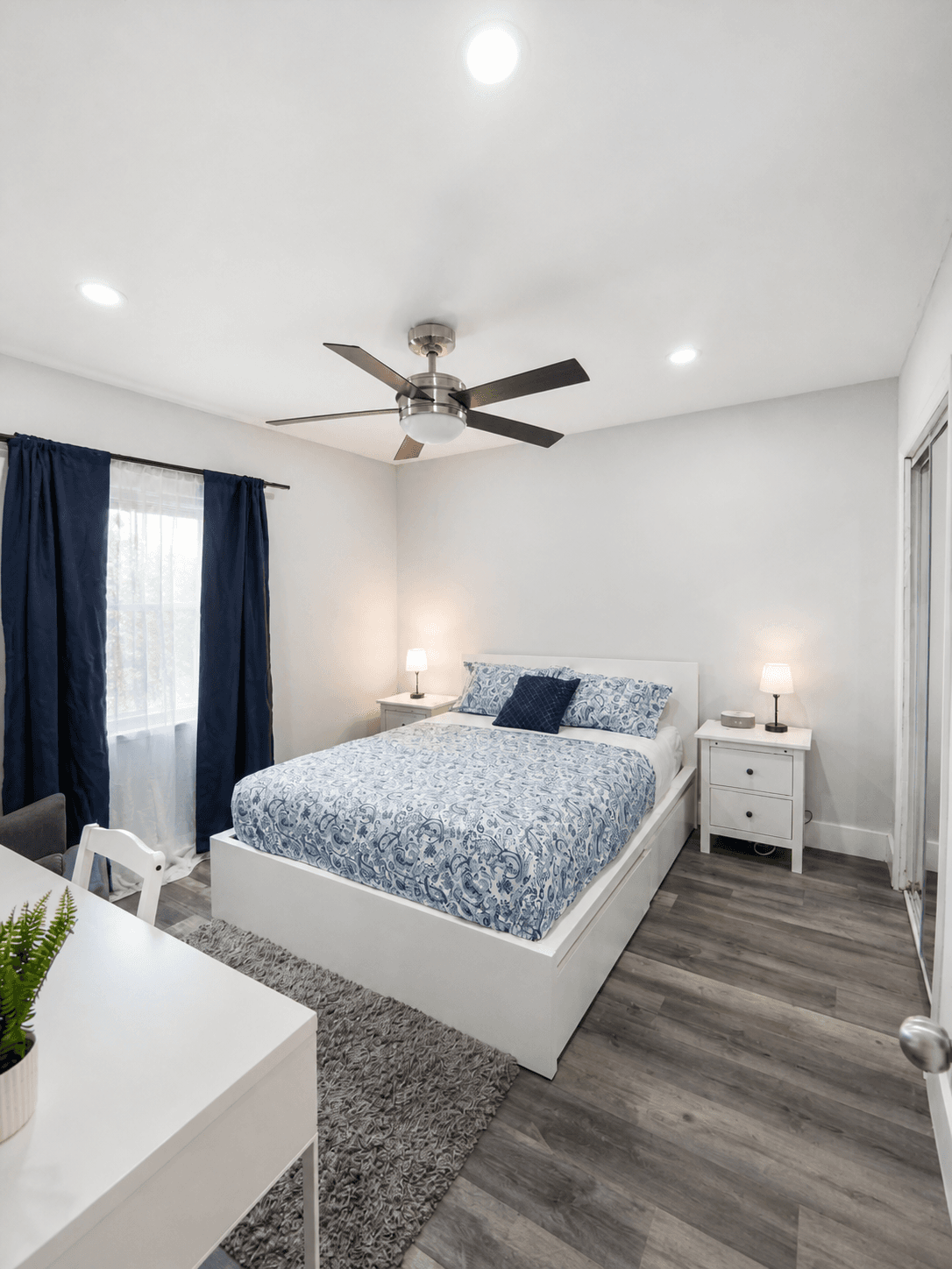 One-bedroom with nightstands, ceiling fan, mirrored closet, and blue-and-white bedding